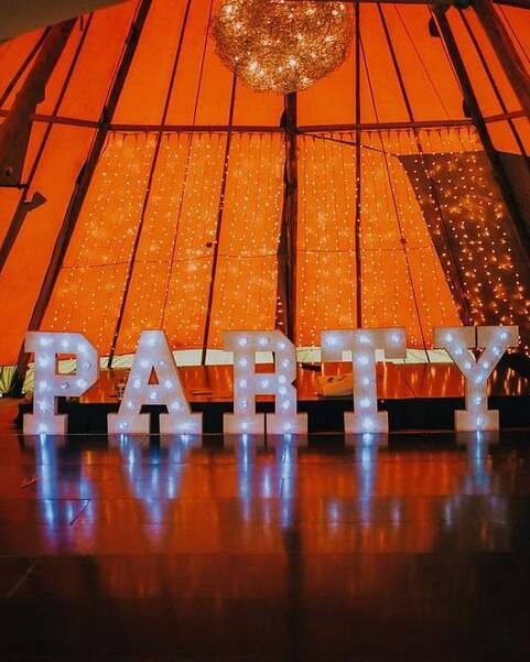 Large Lettered Lights spelling out Party stand in front of staging inside a tipi