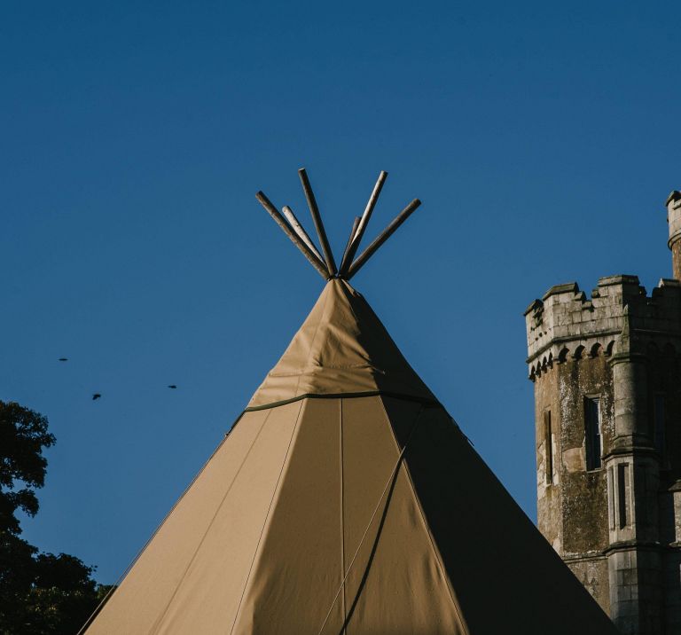 A top of a Tipi stands in front of Narrow Water Castle with a bright blue sky in the background